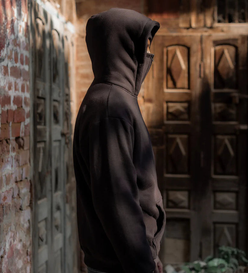 Person wearing a dark hoodie standing against a textured wall with a wooden door.